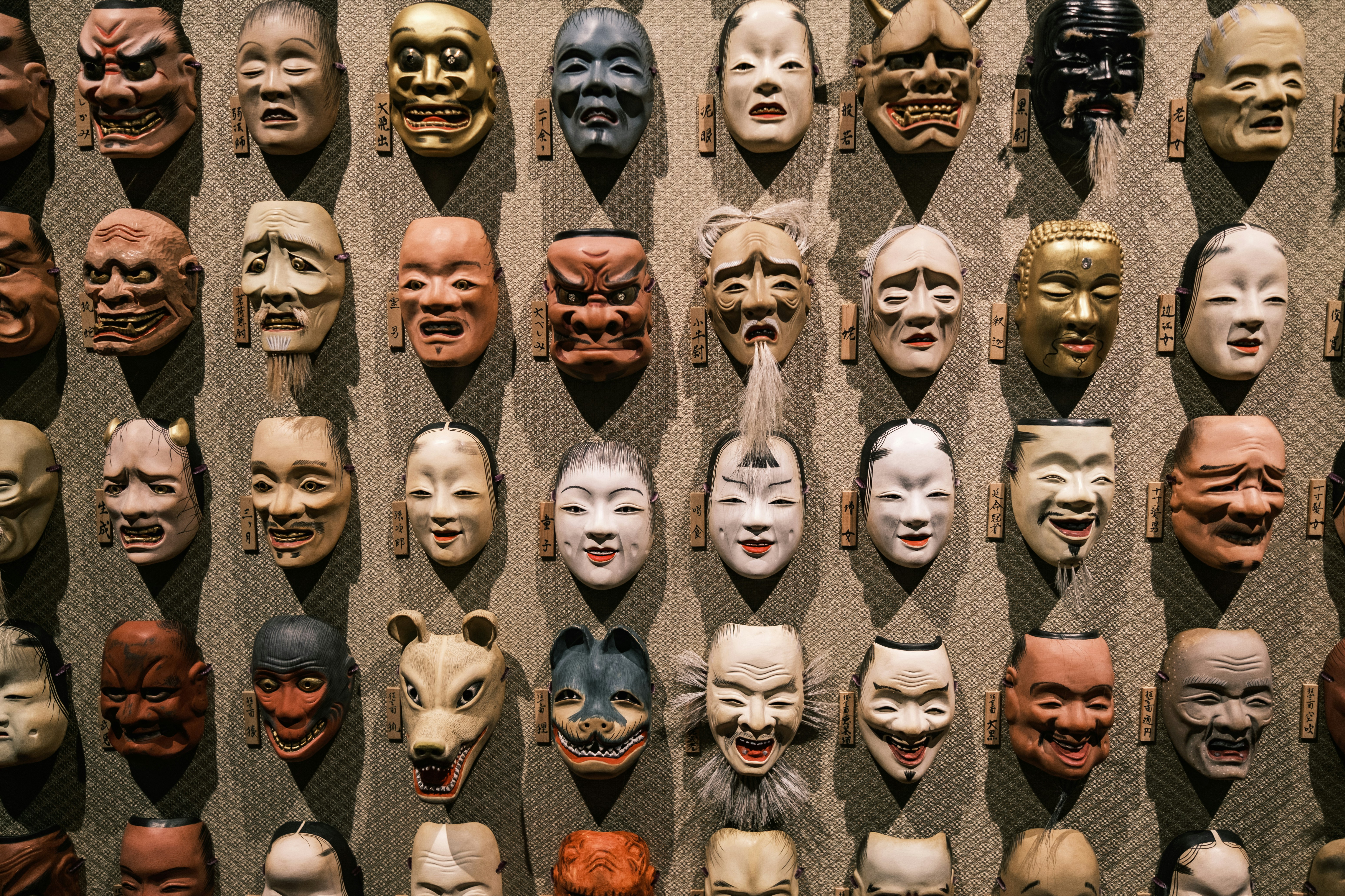 Plus de 32 masques de théâtre japonais exposés sur un mur.